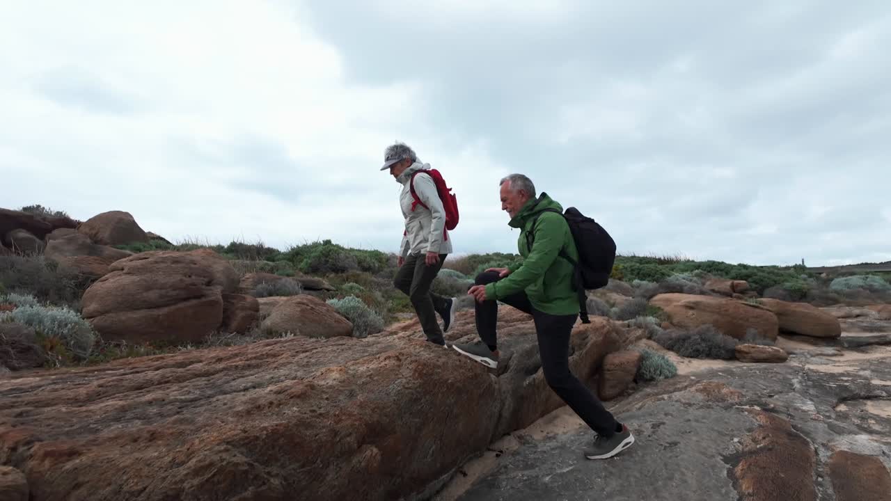 Coppia matura con abbigliamento da trekking che cammina lungo la costa rocciosa nelle vicinanze di Cape Leeuwin