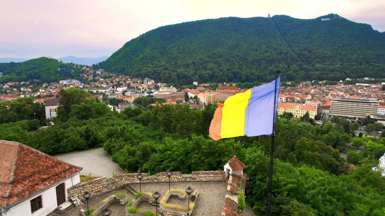 Vista aerea con drone della Cittadella di Brașov, Romania. Fortezza medievale e bandiera nazionale sulla cima di una collina. Edifici e alberi verdi intorno