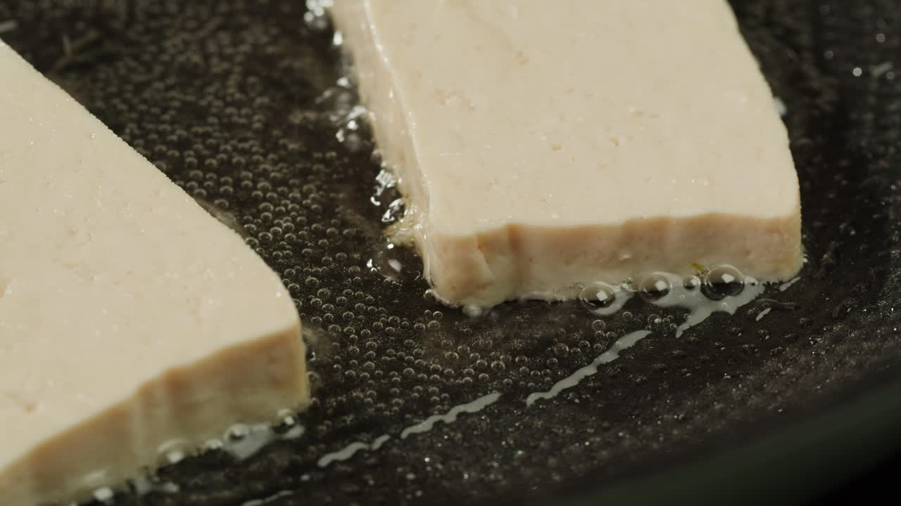 Fried tofu with sesame seeds and spices on cast iron pan, cooking japanese salad. Healthy ingredient for cooking vegan vegetarian diet food. Roasted tofu over black background.
