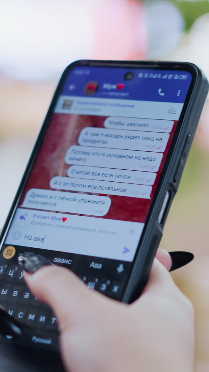 primo piano di un cellulare nero usato per chiacchierare su un tavolo di legno, dita che scrivono sulla tastiera, schermo che mostra messaggi di testo, effetti di luce sfocati intorno