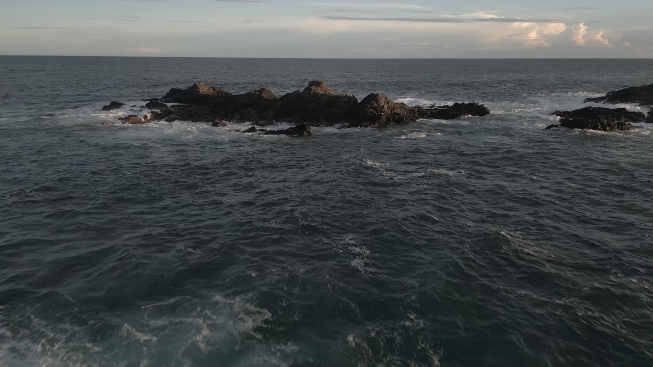 Sorvolo a bassa quota: Onde oceaniche si infrangono contro rocce marine dorate e frastagliate.