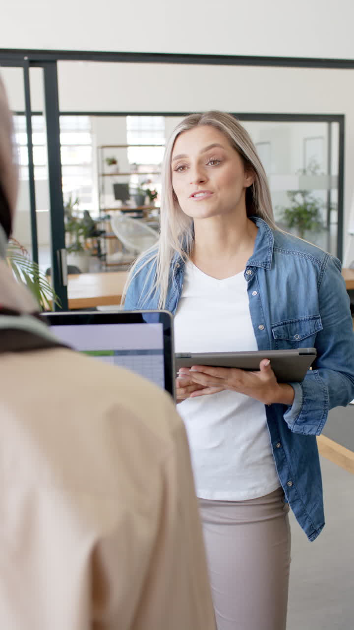 Vertical video of happy diverse business people with tablet talking in office