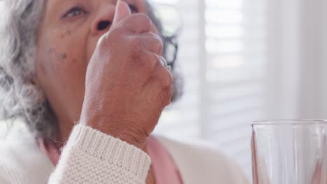 Senior-african-american-woman-sitting-at-table,-taking-pills