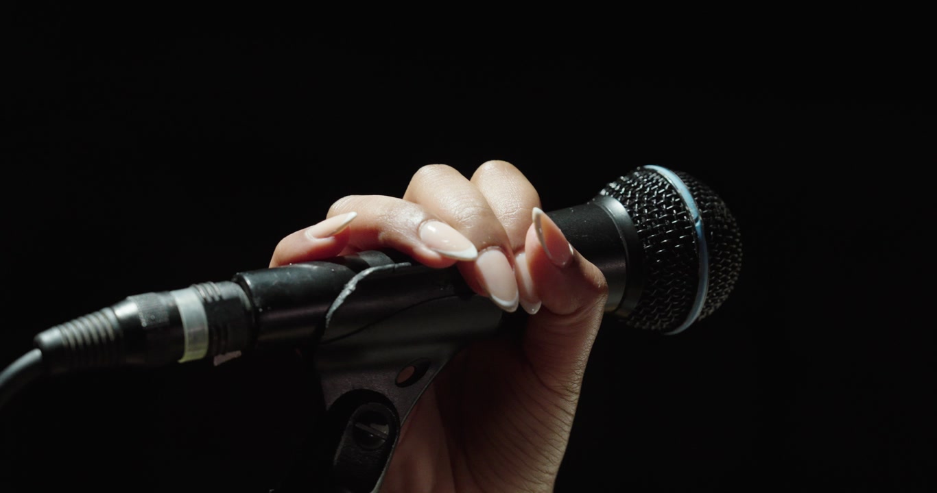 Close-up of a woman’s hand adjusting a microphone against a black background. Concept of music, performance, audio recording and stage preparation.