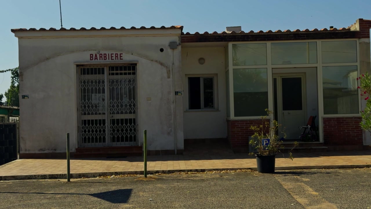 Esterno illuminato dal sole di una classica barberia italiana. La facciata vintage dell'edificio con un'insegna tradizionale si erge sotto un cielo azzurro e limpido