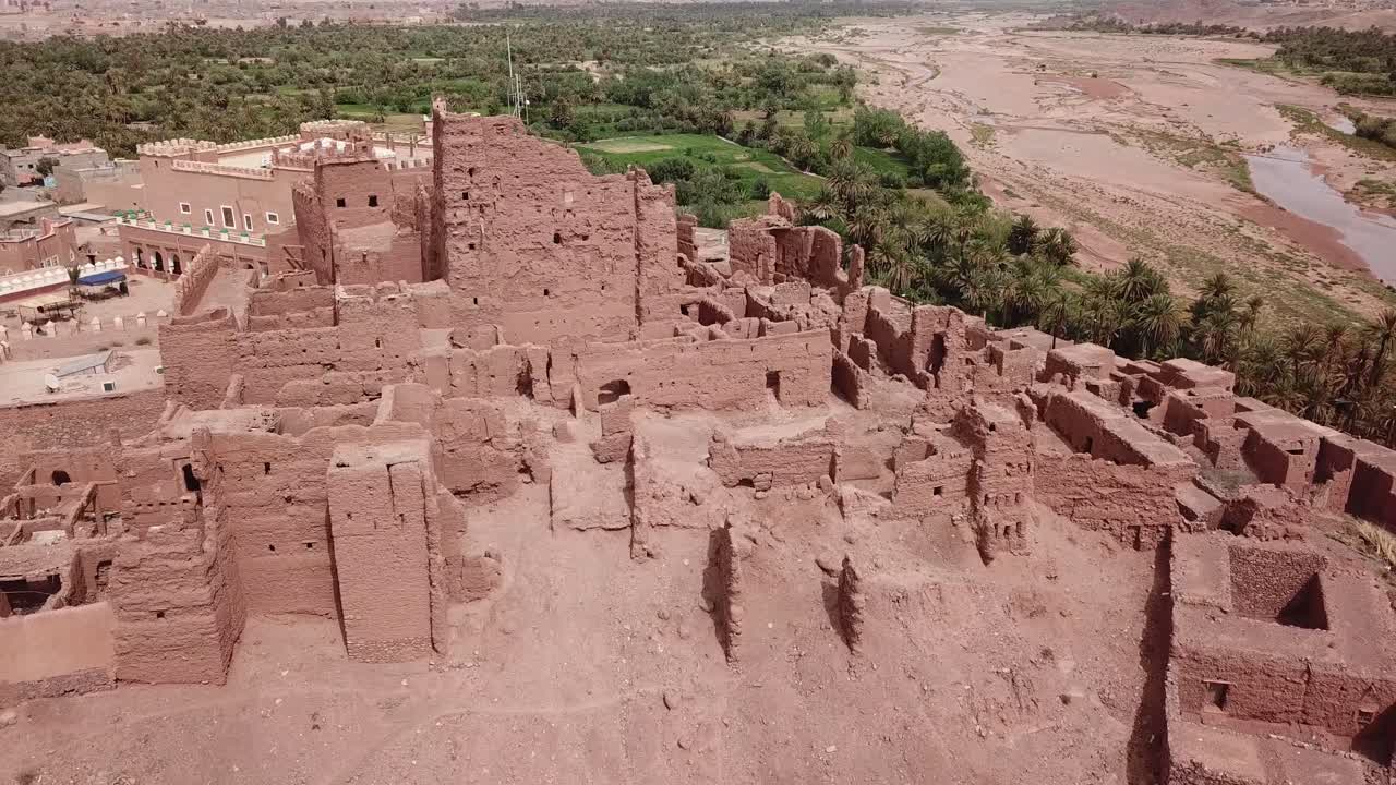 Ilmakuva suuresta Kasbah-kompleksista Ouarzazatessa. Kuvamateriaali esittää monimutkaisia punasavesta tehtyjä raunioita ja kunnostettuja osia, jotka esittelevät perinteistä marokkolaista saviarkkitehtuuria.