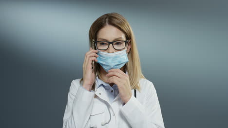 Beautiful-Young-Woman-Doctor-In-Glasses-Taking-Off-Mask-From-Mouth-And-Speaking-Cheerfully-On-The-Phone-And-Smiling