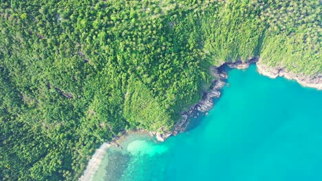 Green-lush-vegetation-of-tropical-island-hills-with-rocky-coastline-washed-by-calm-clear-water-of-turquoise-sea-in-Thailand