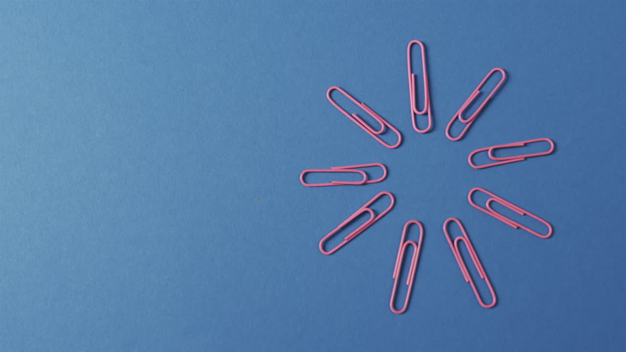vista aérea de clips de papel rosados dispuestos con espacio de copia en fondo azul, en cámara lenta