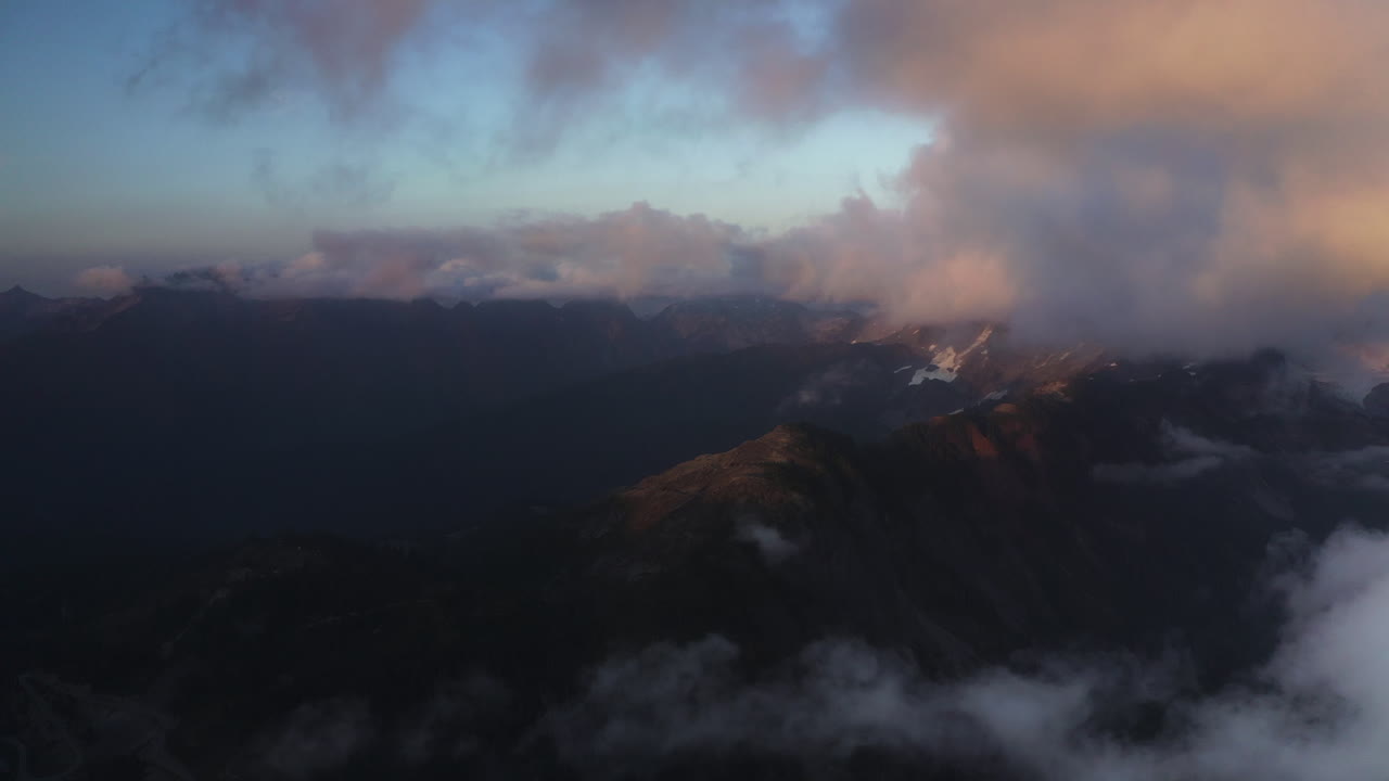 impresionantes nubes suaves de color naranja y púrpura en lo alto del cielo sobre los picos de las montañas al atardecer