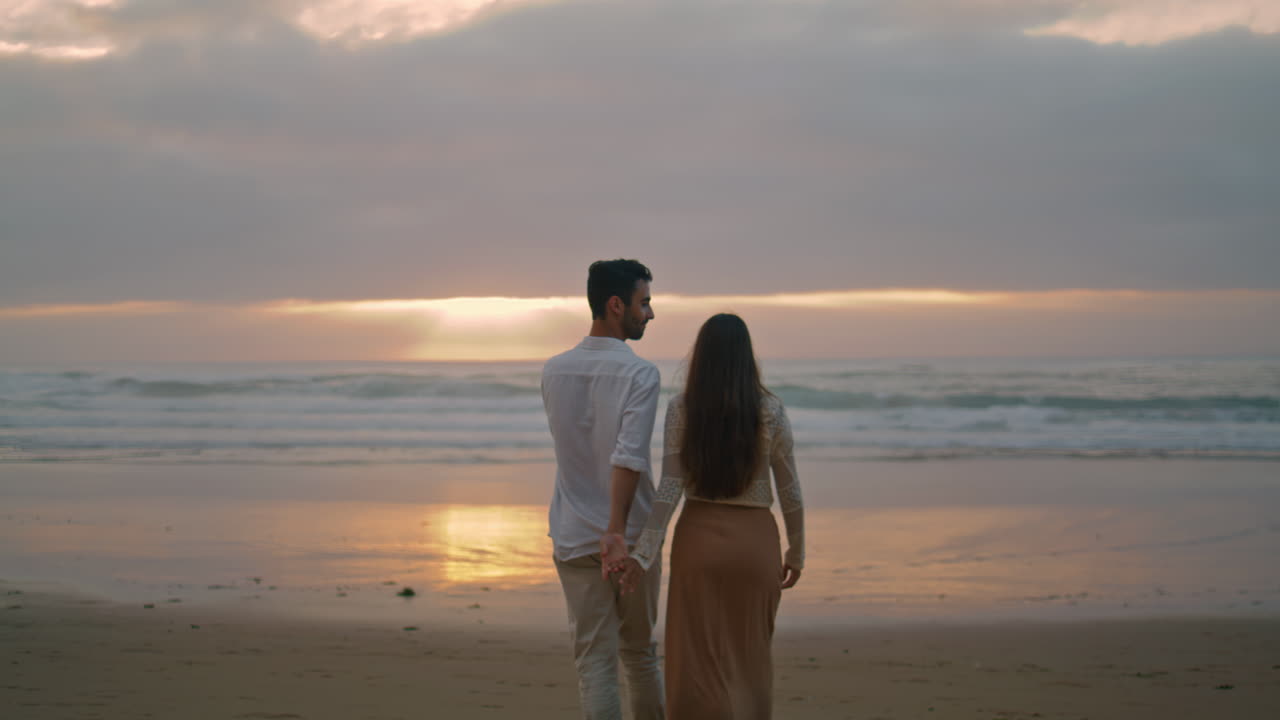 Young spouses relaxing sunbeams beach cloudy evening. Lovers walking vertically