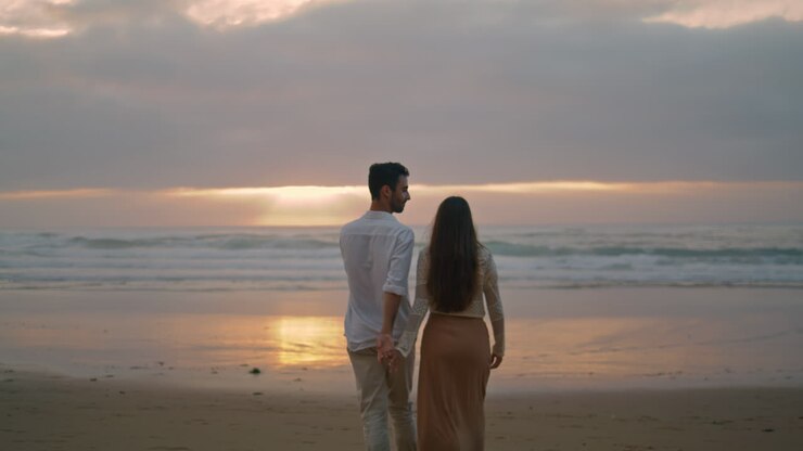 Young spouses relaxing sunbeams beach cloudy evening. Lovers walking vertically