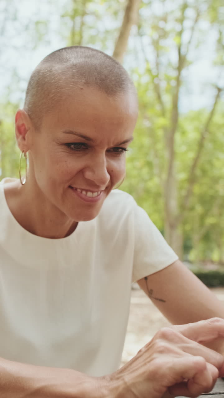 Donna calva sorridente che usa lo smartphone all'aperto in un parco