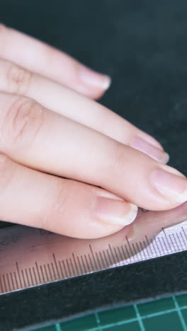 cu: woman hand cuts black leather strip with special rotary cutter near large metal ruler extreme close view
