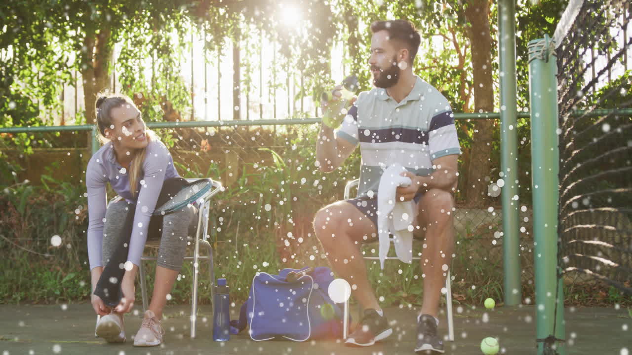 Sitting on tennis court bench, two people drinking water and watching animation
