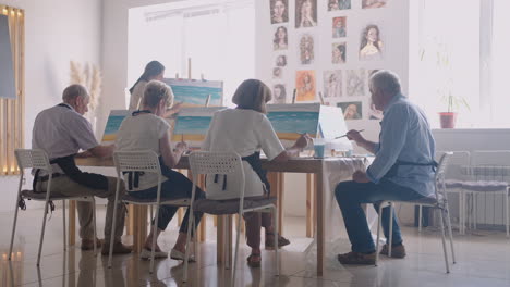 side view of a happy senior people smiling while drawing as a recreational activity or therapy in paint class together with the group of retired women and men