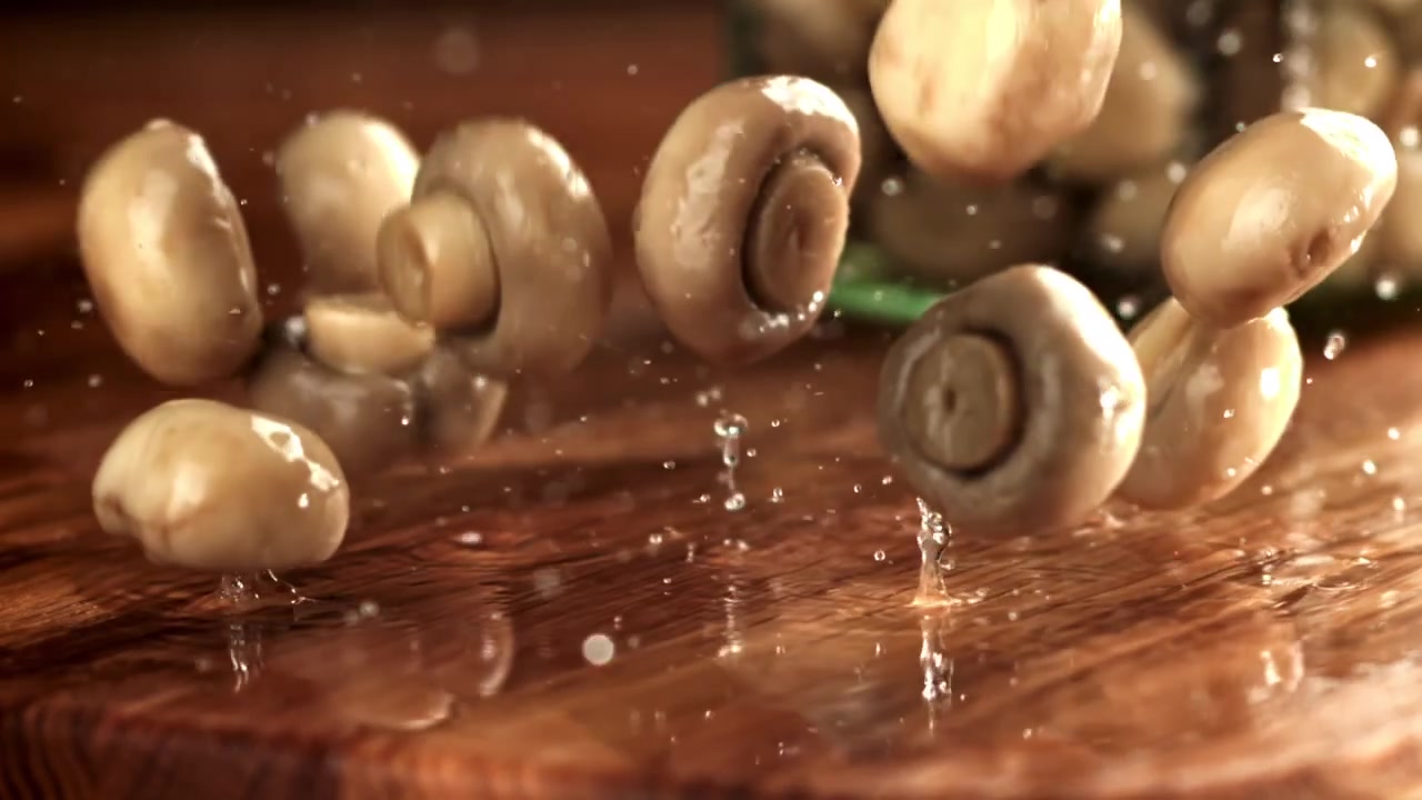 Friske champignoner falder og sprøjter ned på en våd træoverflade i slowmotion.