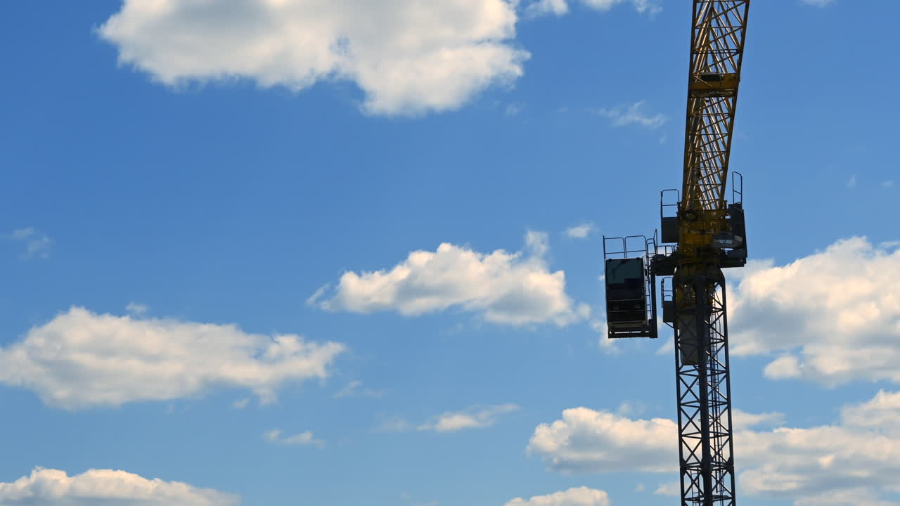 Time lapse of a tower crane working under bright blue sky with white clouds