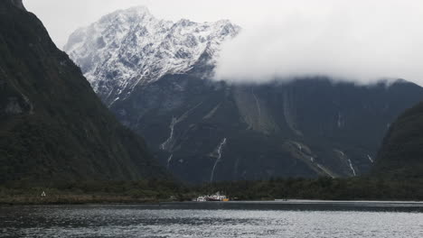 barcos anclados frente a un enorme acantilado cubierto de nieve, milford sound, nueva zelanda