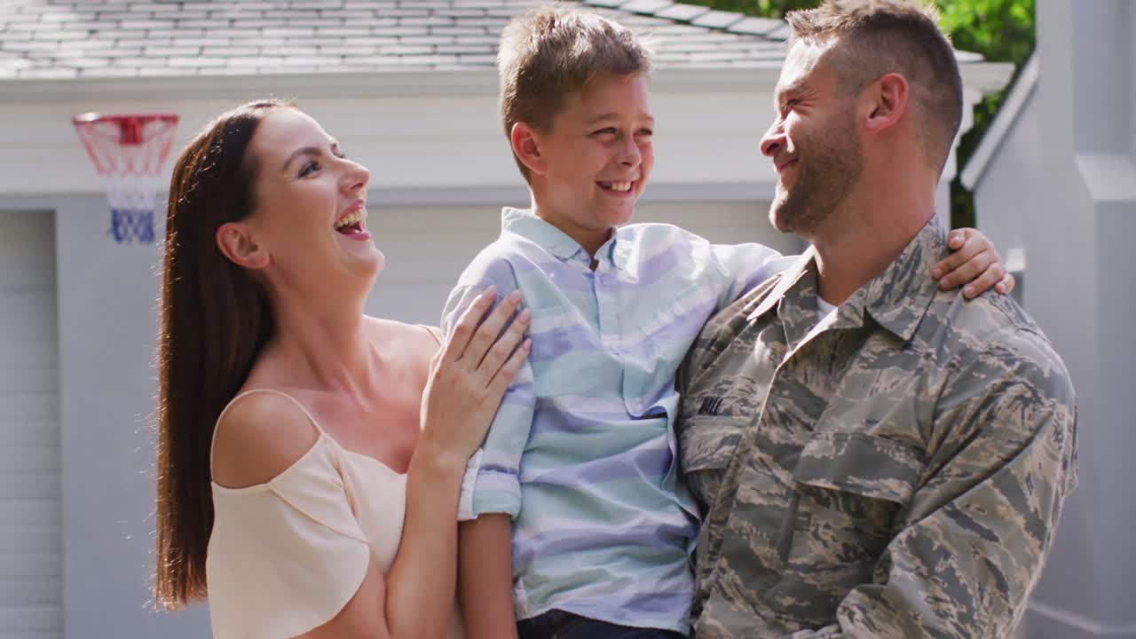 행복 한 백인 남성 군인 은 그 들 의 집 밖 의 정원 에서 아내 와 함께 웃는 아들 을 품고 있다