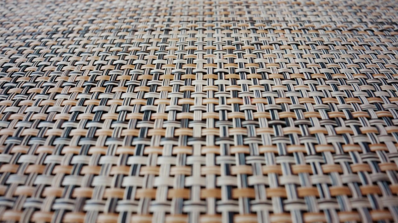 A detailed macro shot of a woven material reveals an intricate pattern of interlaced fibers in neutral tones