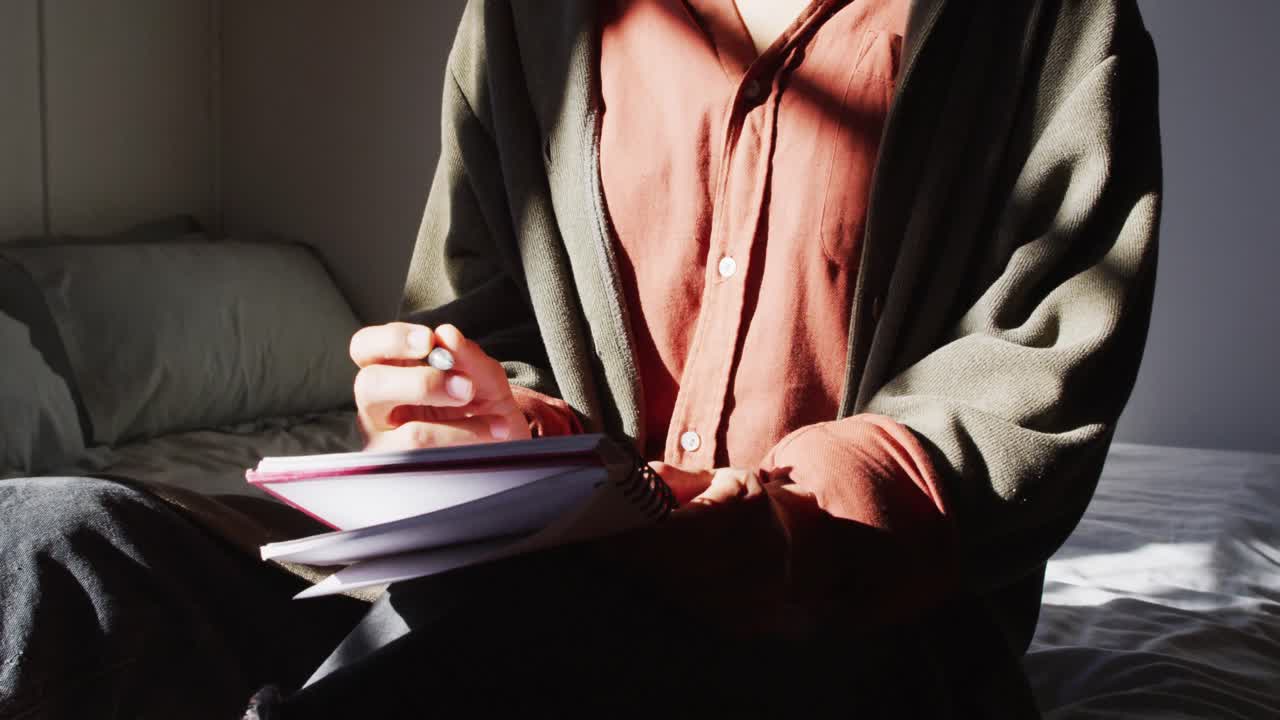 사려 깊은 혼합 인종의 여성이 침대에 앉아  ⁇ 은 오두막 침실에서 쓰고 있습니다.