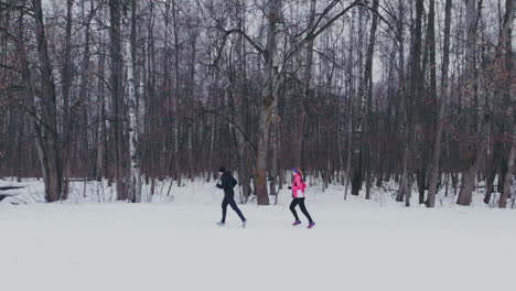 man and woman in the winter running through the park in slow motion.