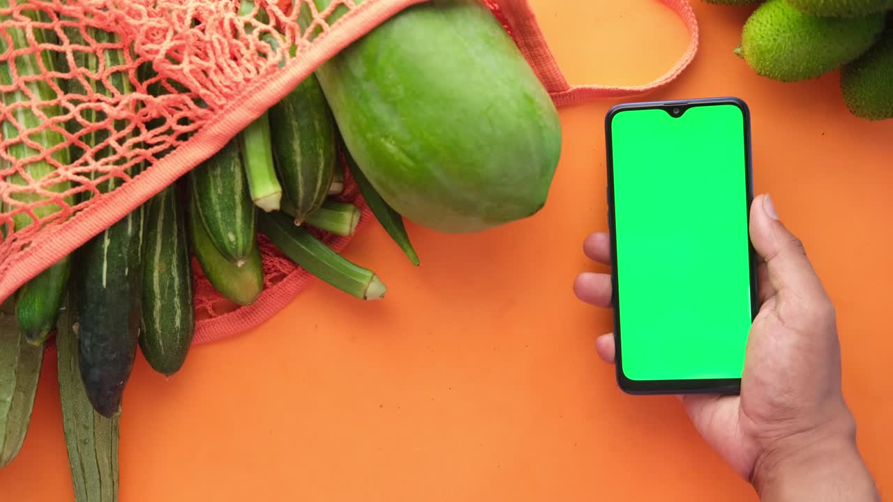 vista superior de la mano del hombre sosteniendo un teléfono inteligente con verduras frescas en la mesa