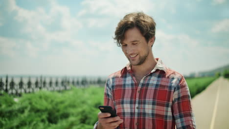 Happy-man-using-smartphone-outside.-Smiling-guy-walking-on-road-in-park