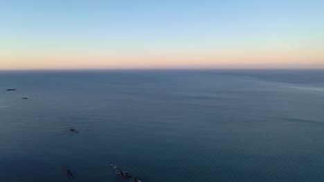 Beautiful-aerial-panning-shot-from-the-sea-into-snow-covered-flatland-and-mountains-at-dusk