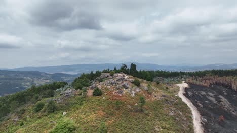 Aerial-drone-shot-over-a-mountain-peak-with-part-of-natural-green-vegetation-destroyed-due-to-bush-fire-in-Galicia,-Spain-on-a-cloudy-day