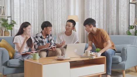 asian teen group studying at home. students with a laptop and books writing into notebook, celebrating success in project, giving high five gesture