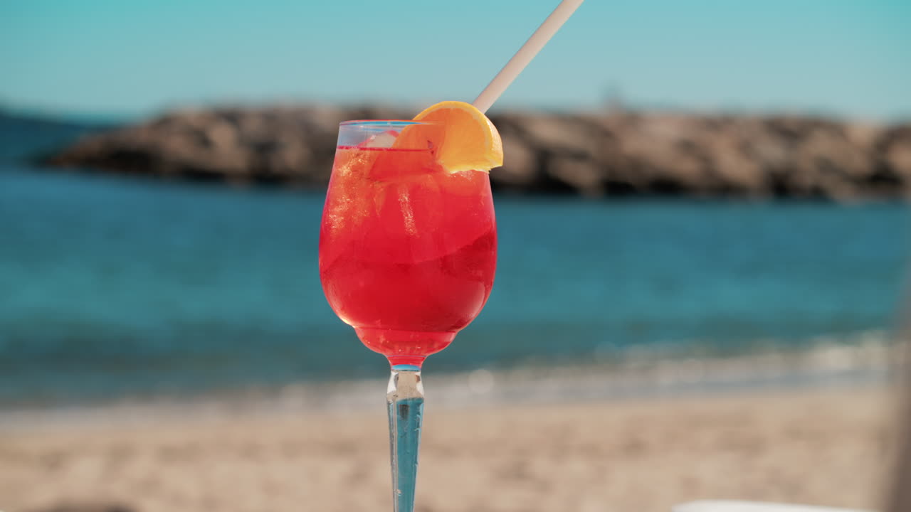 Un cocktail rinfrescante rosso-arancio con ghiaccio e fetta d'arancia sullo sfondo del blu intenso del Mar Mediterraneo
