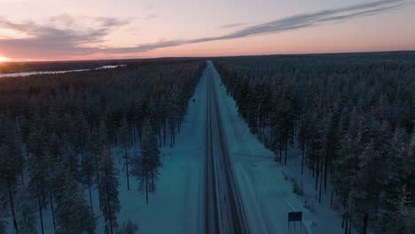 aerial of winter road between dense thicket during sunset in finland