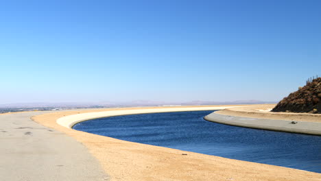 sliding shot of the california aqueduct full of blue water supply heading into los angeles during a drought