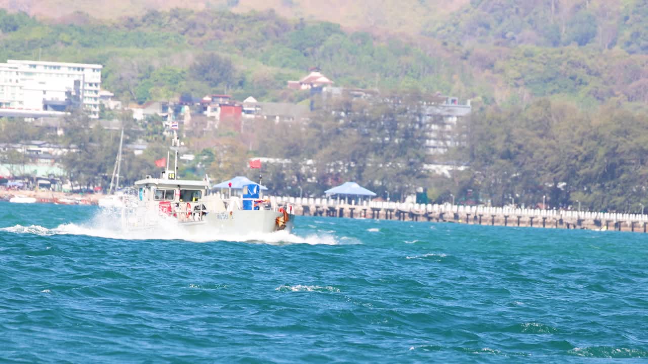 A patrol boat moves swiftly across the ocean near Phuket, Thailand, under clear skies, showcasing maritime activity