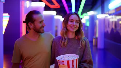 happy young caucasian woman and man walking by cinema hall, hugging and chatting