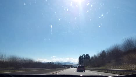 Fahren-Sie-Im-Zeitraffer-Auf-Einer-Autobahn-Mit-Tunneln,-Die-An-Anderen-Autos-Vorbeifahren,-Die-An-Einem-Sonnigen-Tag-Mit-Blauem-Himmel,-Grasbewachsenen-Feldern-Mit-Bäumen-Und-Schneebedeckten-Bergen-In-Der-Ferne-Fahren