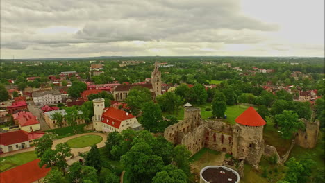 Vista-Aérea-Del-Castillo-De-Cēsis-Que-Captura-La-Icónica-Fortaleza-Medieval-Y-El-Paisaje-Urbano-Circundante-A-La-Luz-Del-Día-En-Letonia,-En-Medio-De-Cielos-Nublados.