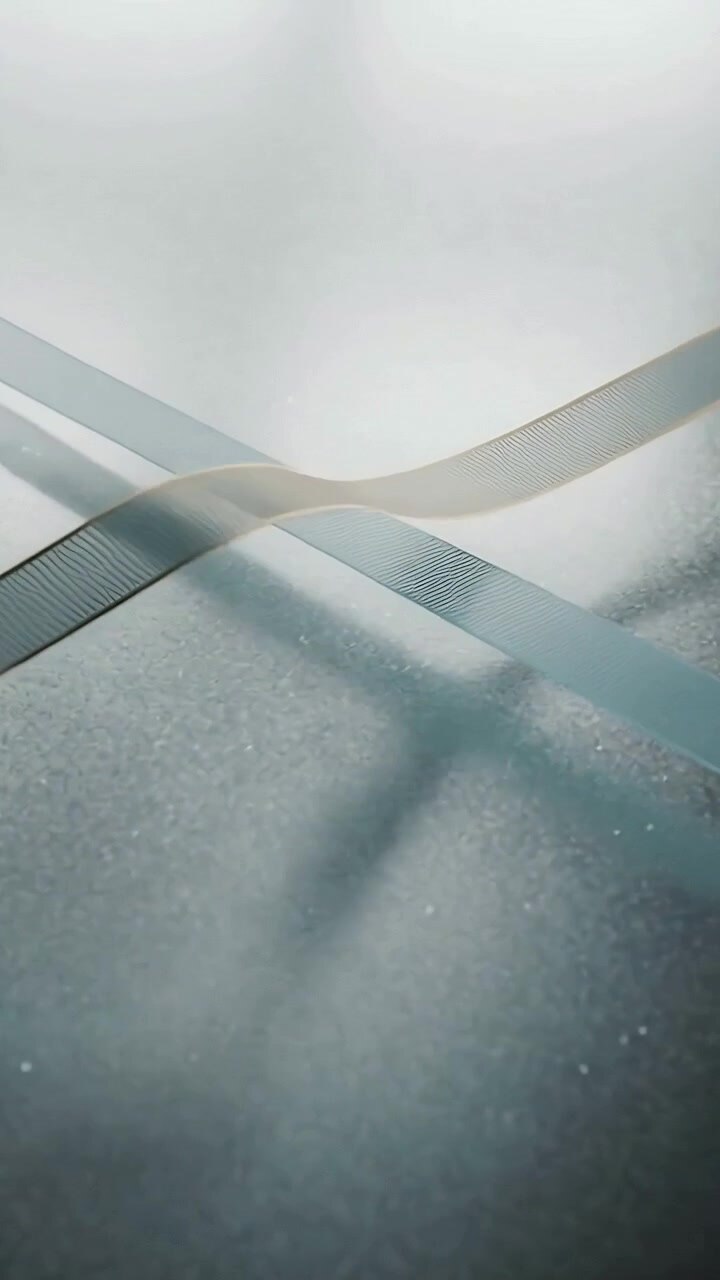 Vertical video: Shifting light nudging pale blue and beige ribbons sliding on table, catching light