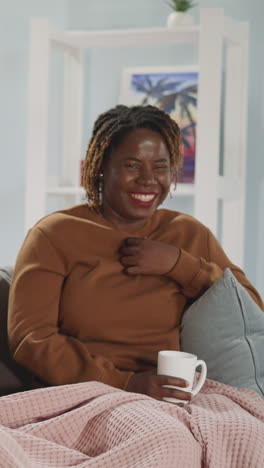 african american woman laughs looking at embarrassed indian girl friend while watching comedy. multiracial female friends spend evening together at home