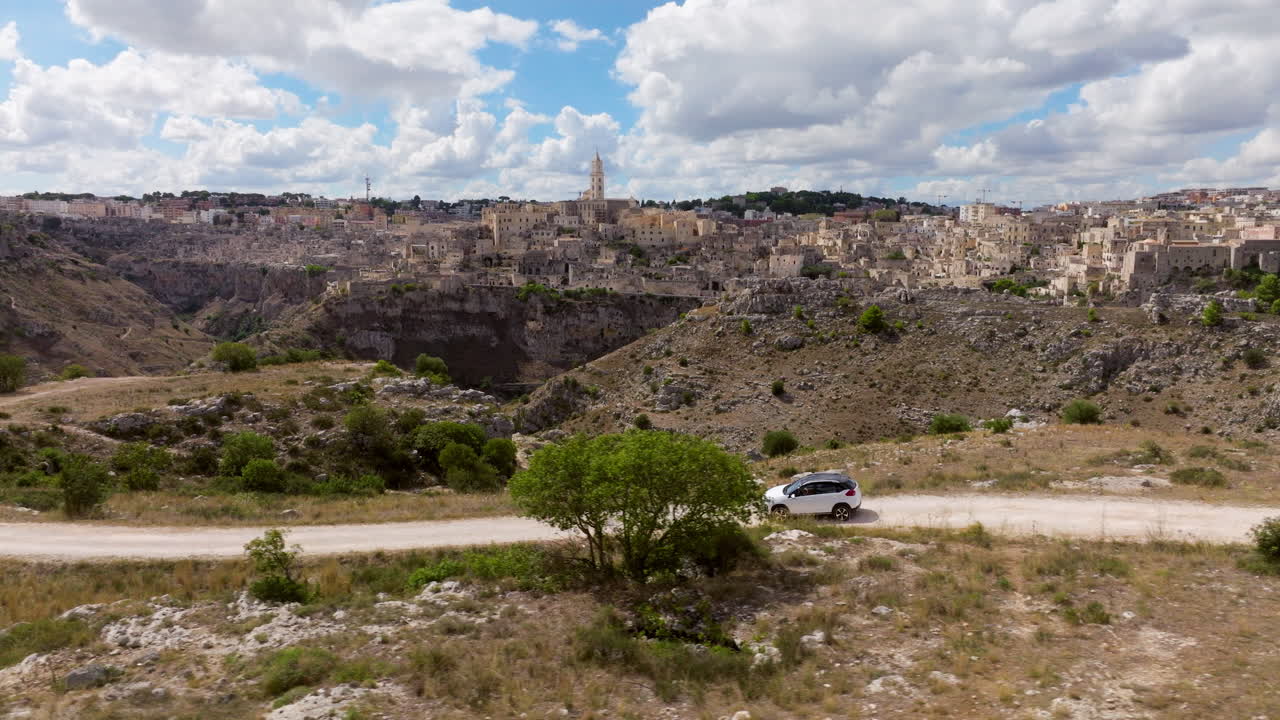 Aerial View Of A Car Driving On Dirt Road With Matera City Background In Basilicata, Southern Italy.