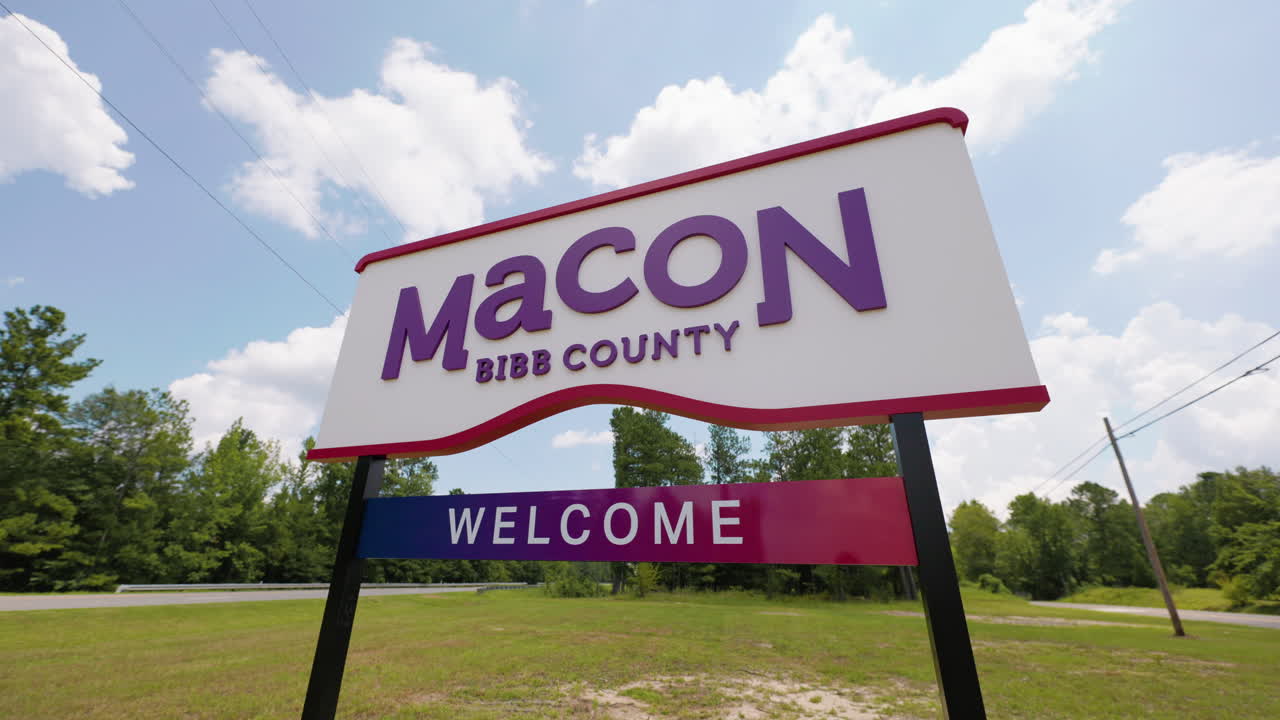 macon bibb condado de georgia bienvenida cartel de carretera en frente de la carretera camino bosques gran ángulo pan a la izquierda soleado cielo de verano nubes 60p 0003