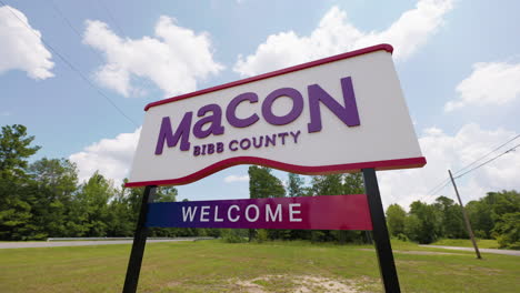 Macon-Bibb-County-Georgia-welcome-road-sign-in-front-of-highway-road-woods-wide-angle-pan-left-sunny-summer-sky-clouds-60p-0003