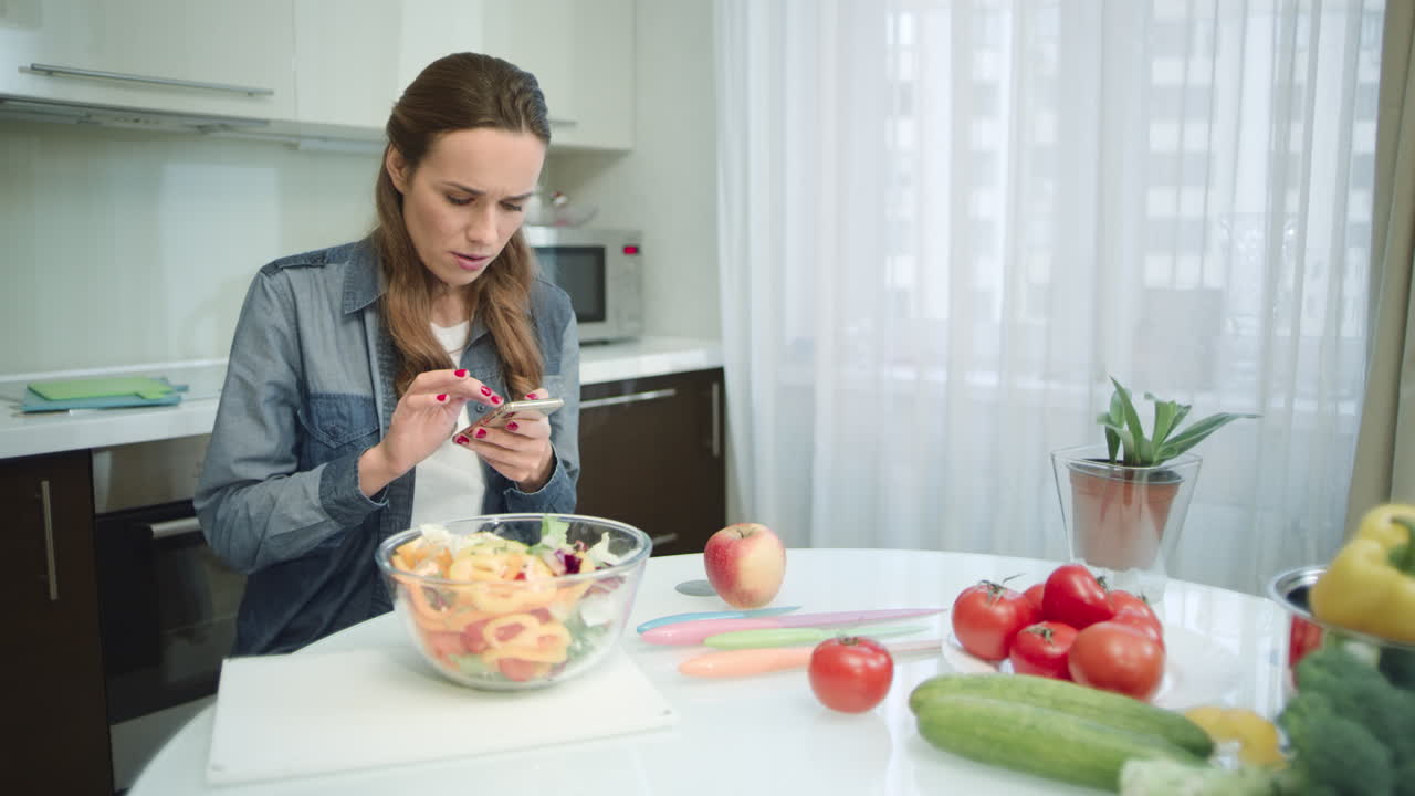 Woman using mobile phone in modern kitchen. Housewife looking for recipe.