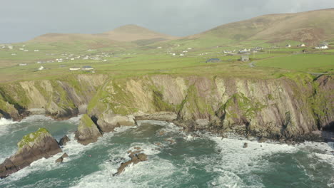 Aerial-view,-Dunquin-Pier-is-situated-in-a-small-secluded-bay-surrounded-by-rocky-cliffs,-famous-postcard-image-of-Ireland,-surrounding-landscape-is-an-attractive-mixture-of-mountain-and-cliff-top