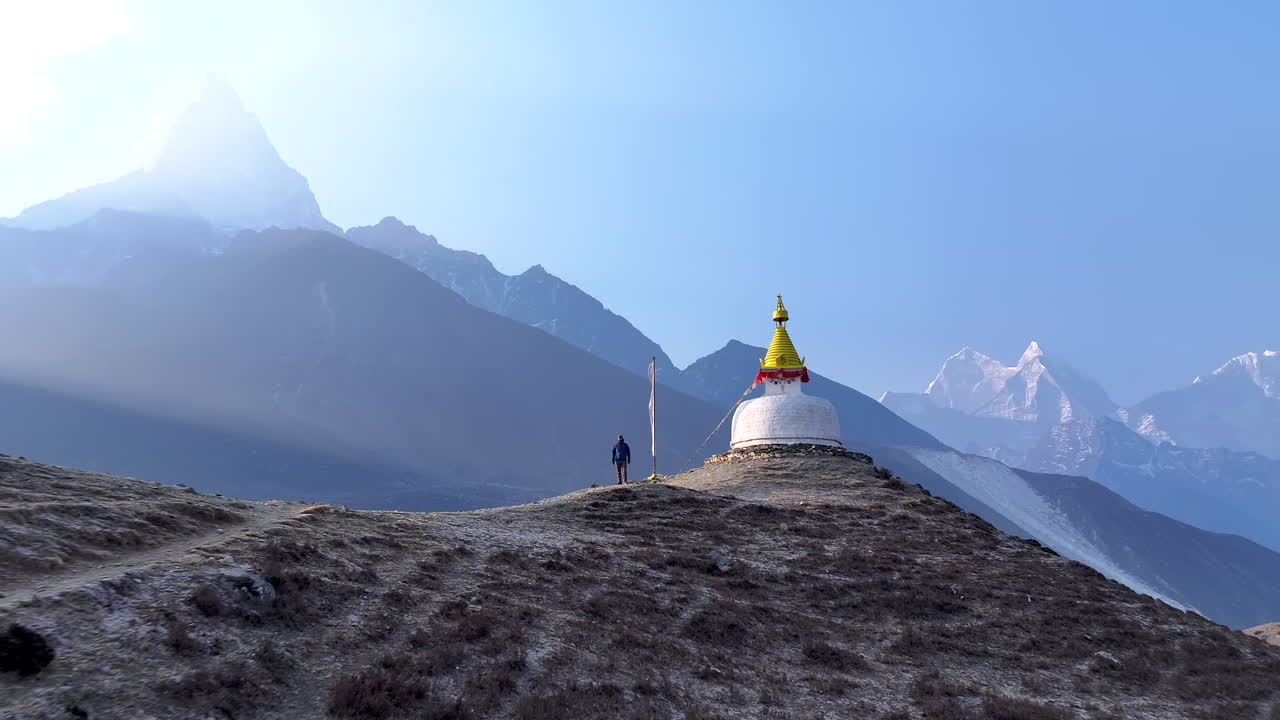Drone shot of male tourist in awe at Buddhist stupa in Dingboche, Khumbu region, Nepal. Ama Dablam peak Himalayan ranges form peaceful, spiritual backdrop Everest Base Camp trek, sunrays and serenity