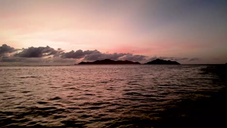 Vista-Aérea-De-La-Puesta-De-Sol-Brillando-Sobre-El-Océano-Con-Islas-Y-Nubes-Distantes