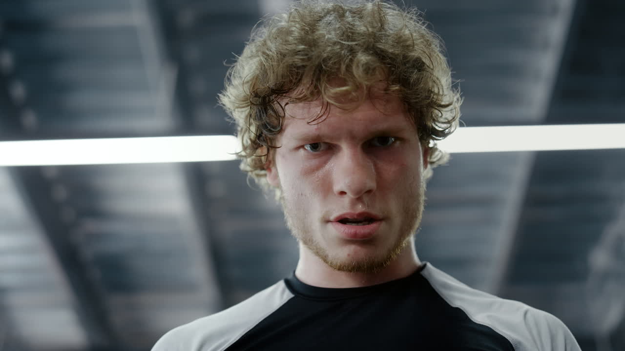 красивый боец смотрит на объектив в спортивном клубе. кикбоксер делает перерыв в тренажерном зале