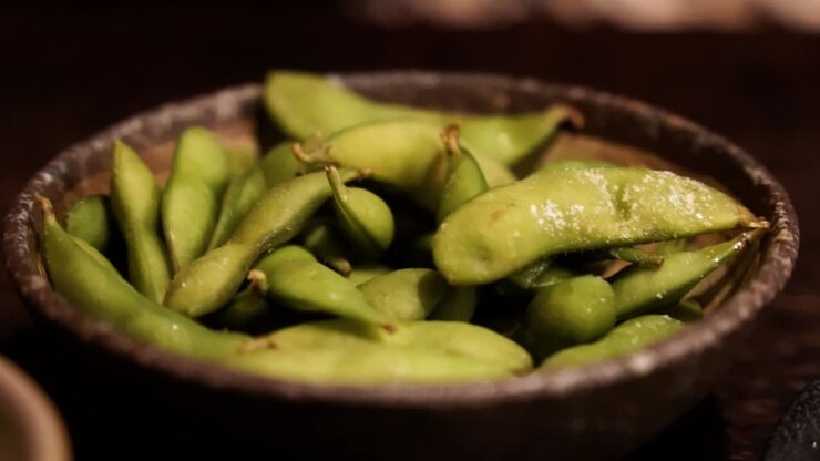 Hand picking up from bowl of edamame beans
